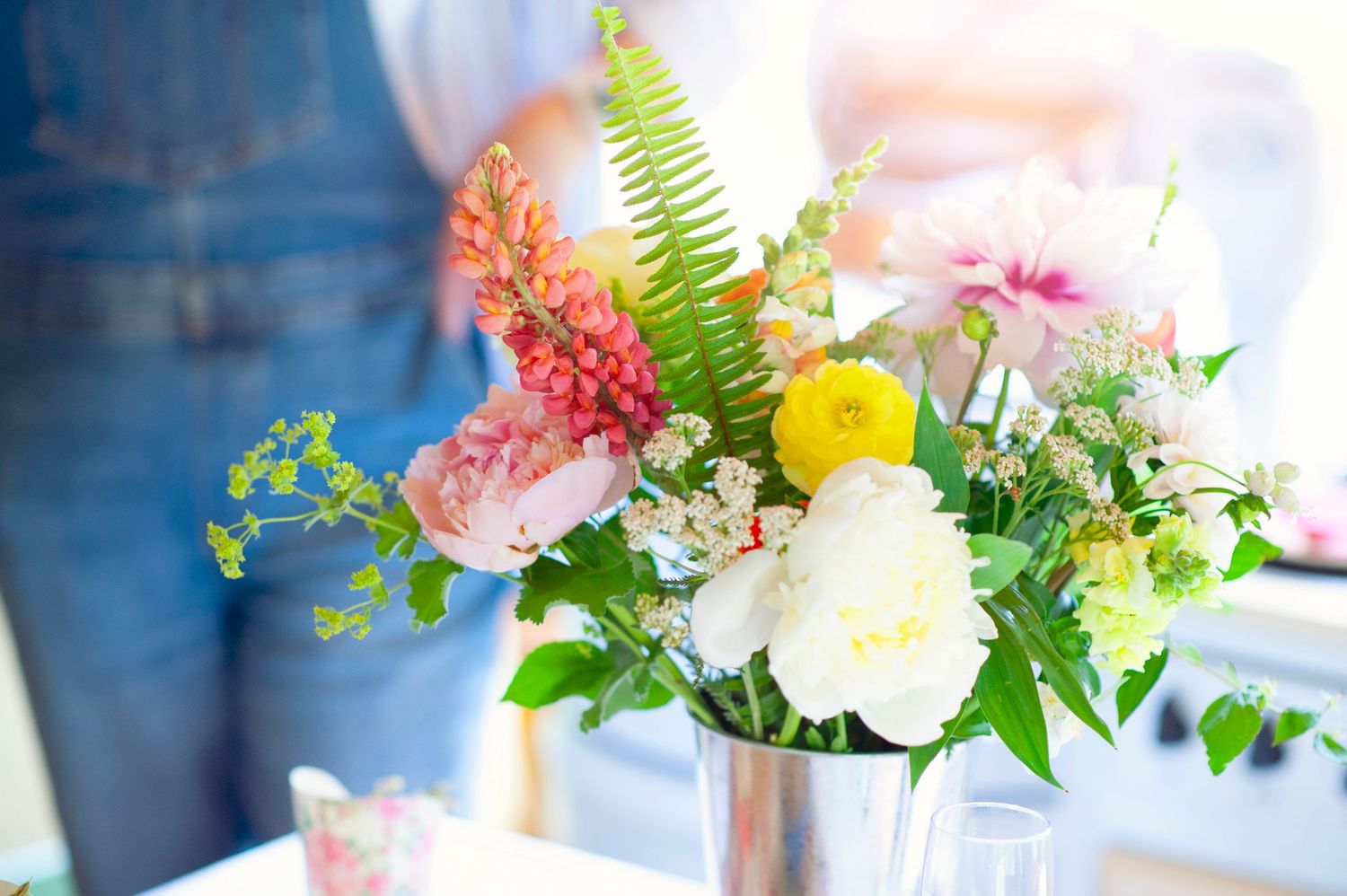 Bright spring flower arrangement with peonies, yellow blooms, and ferns in a silver vase at a workshop.