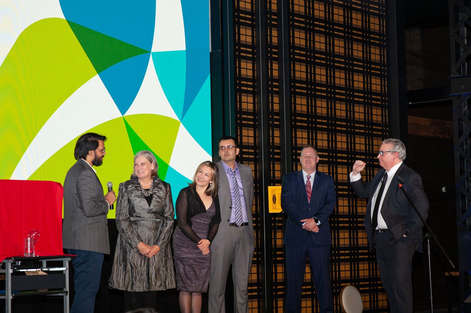 Group of seven people stand on stage during an awards ceremony presentation.