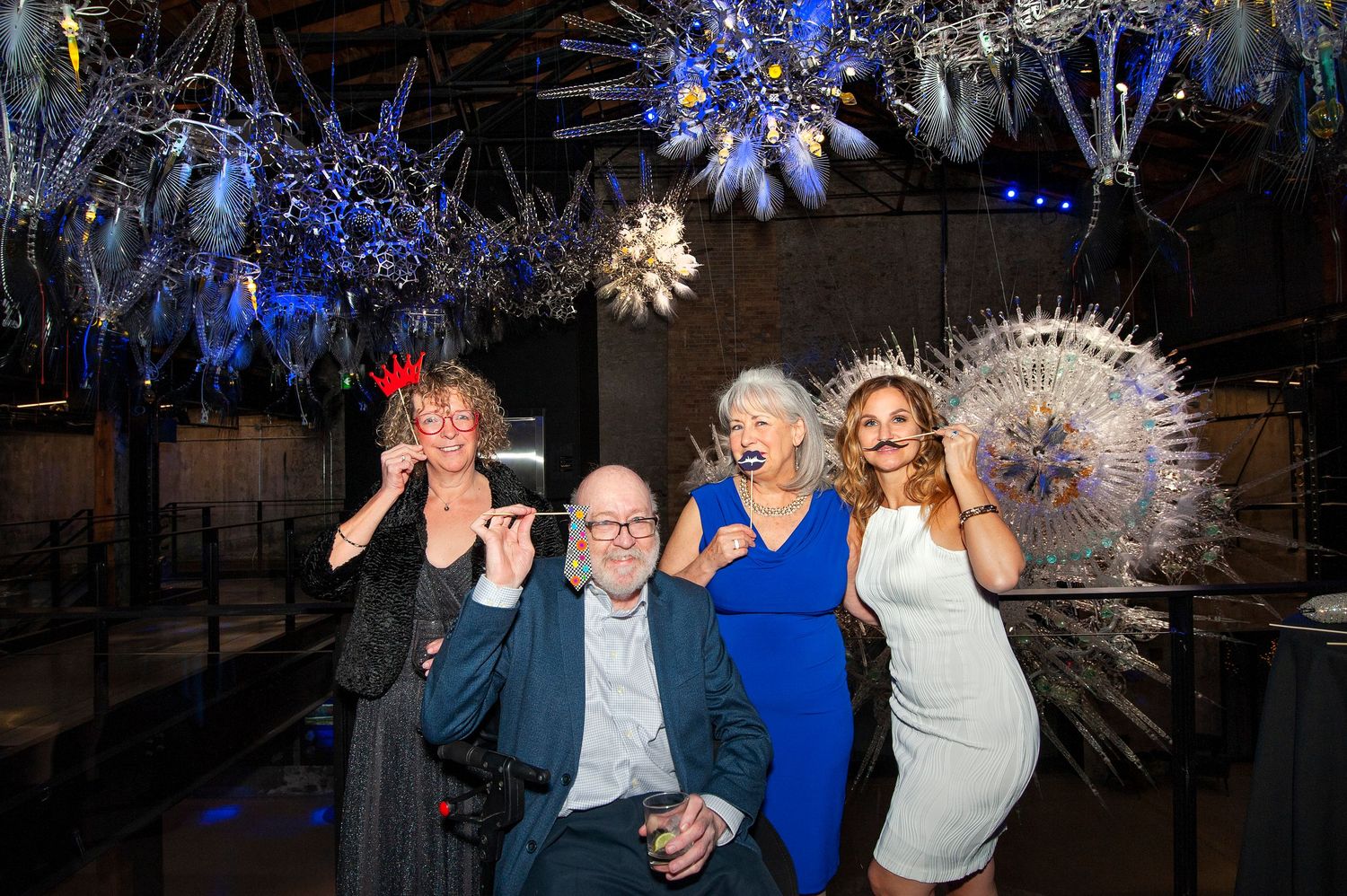 Four guests posing playfully under decorative spiky white sculptures at a festive indoor gala.