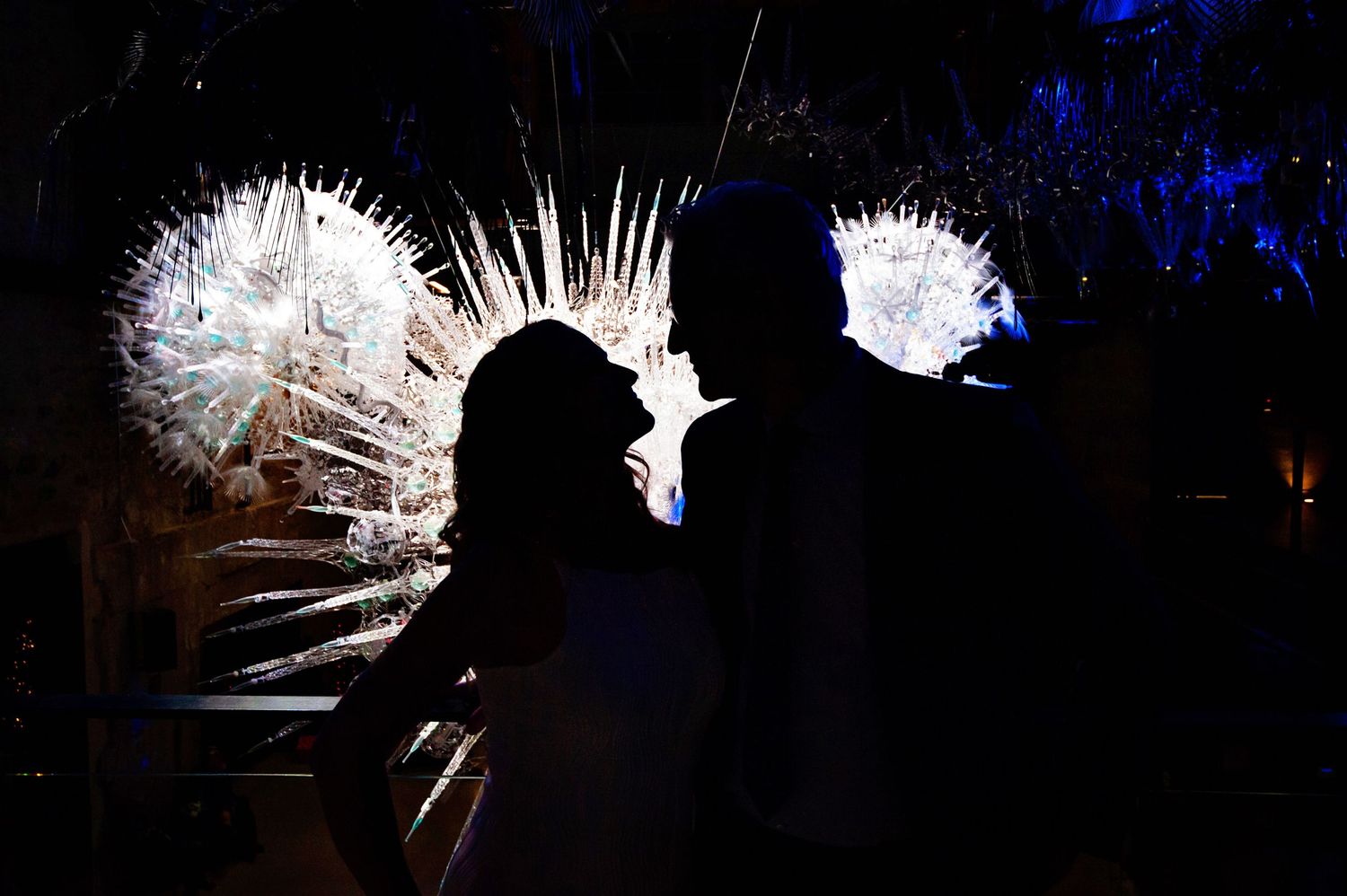Romantic silhouette of couple against glowing white floral installation at night event.
