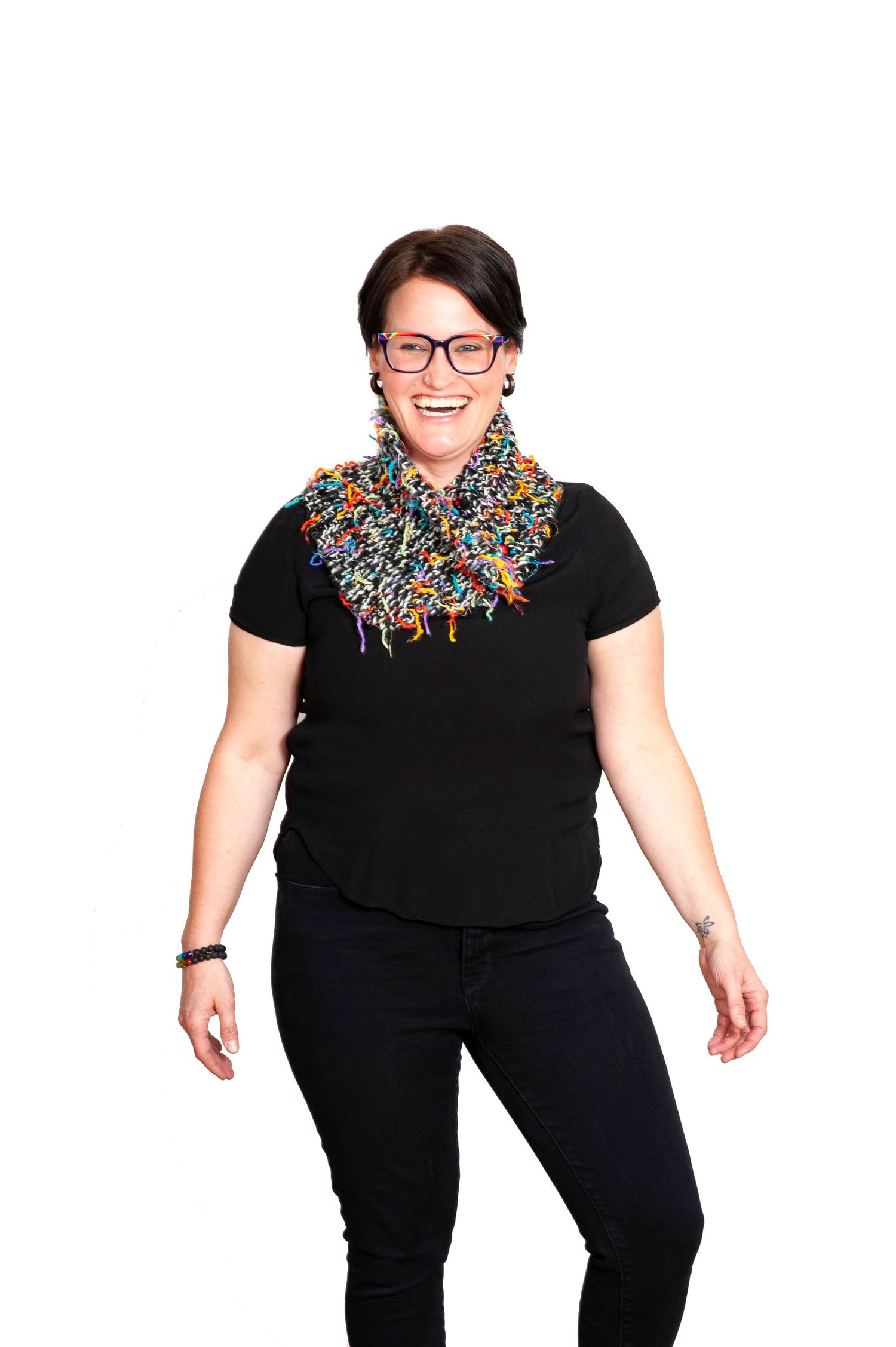 Woman in black outfit wearing a colorful fringe scarf laughing on white background.