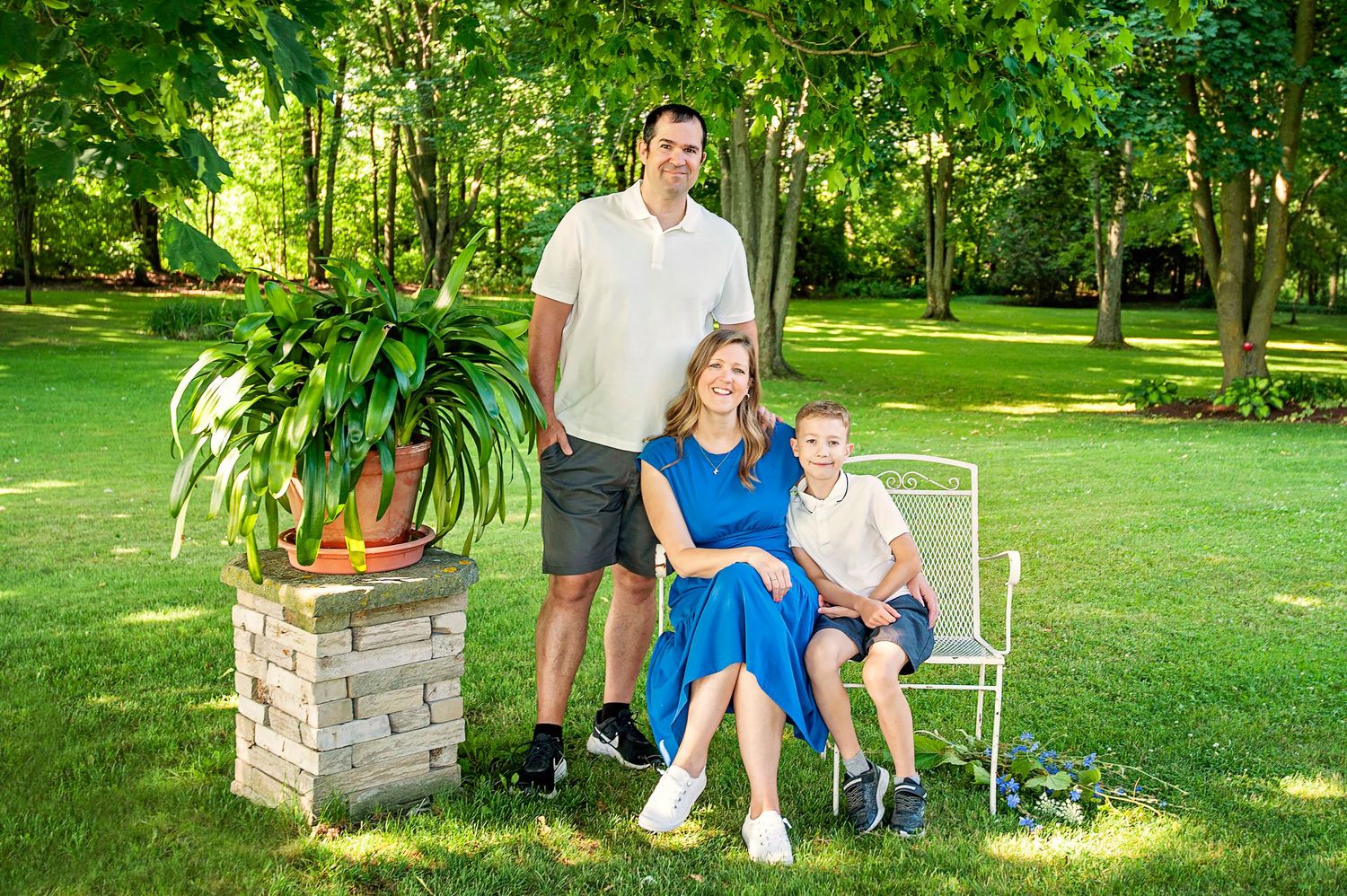 Family of three smiling together in lush green backyard garden during summer.
