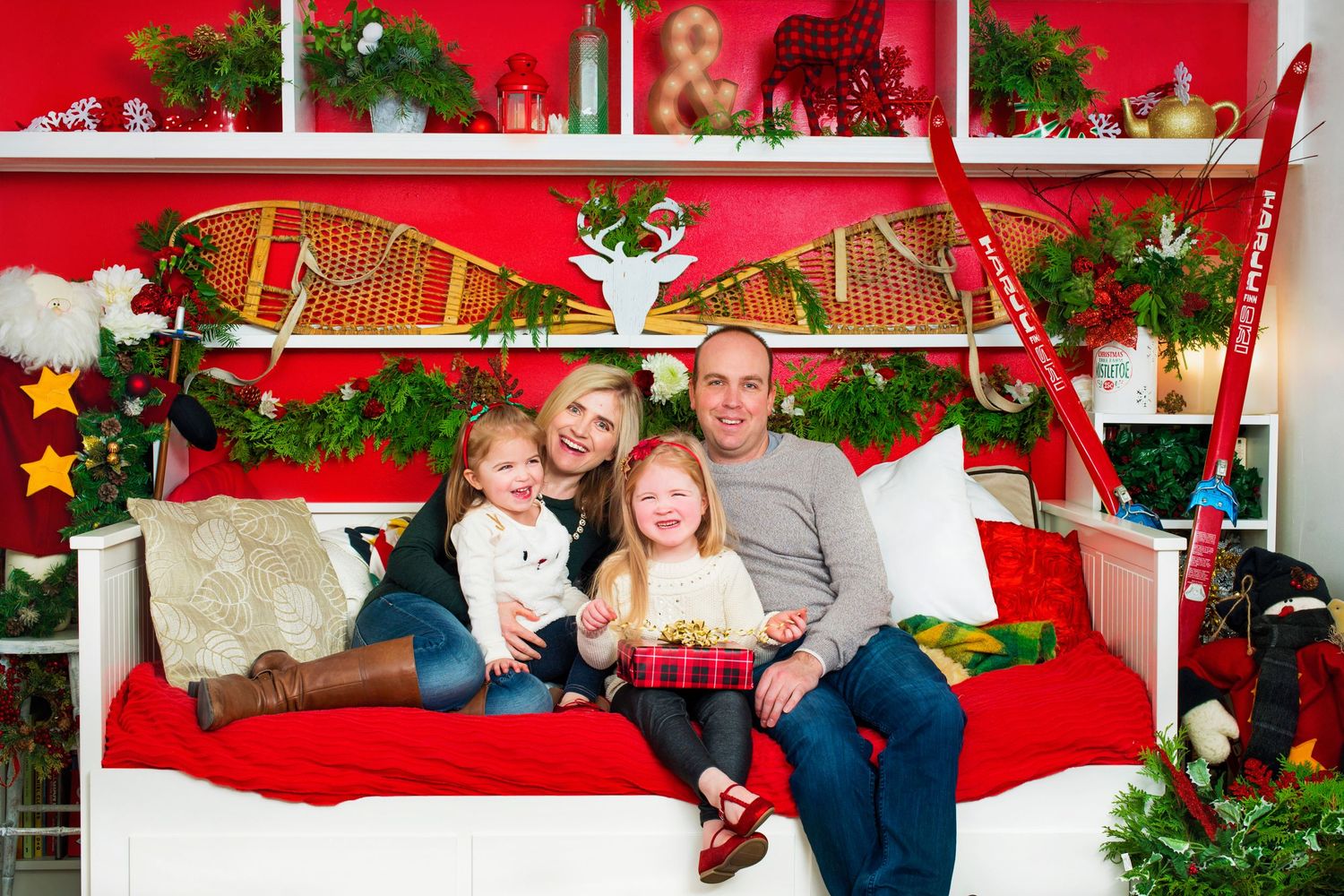Family of four posing together in festive Christmas holiday decorated red room.