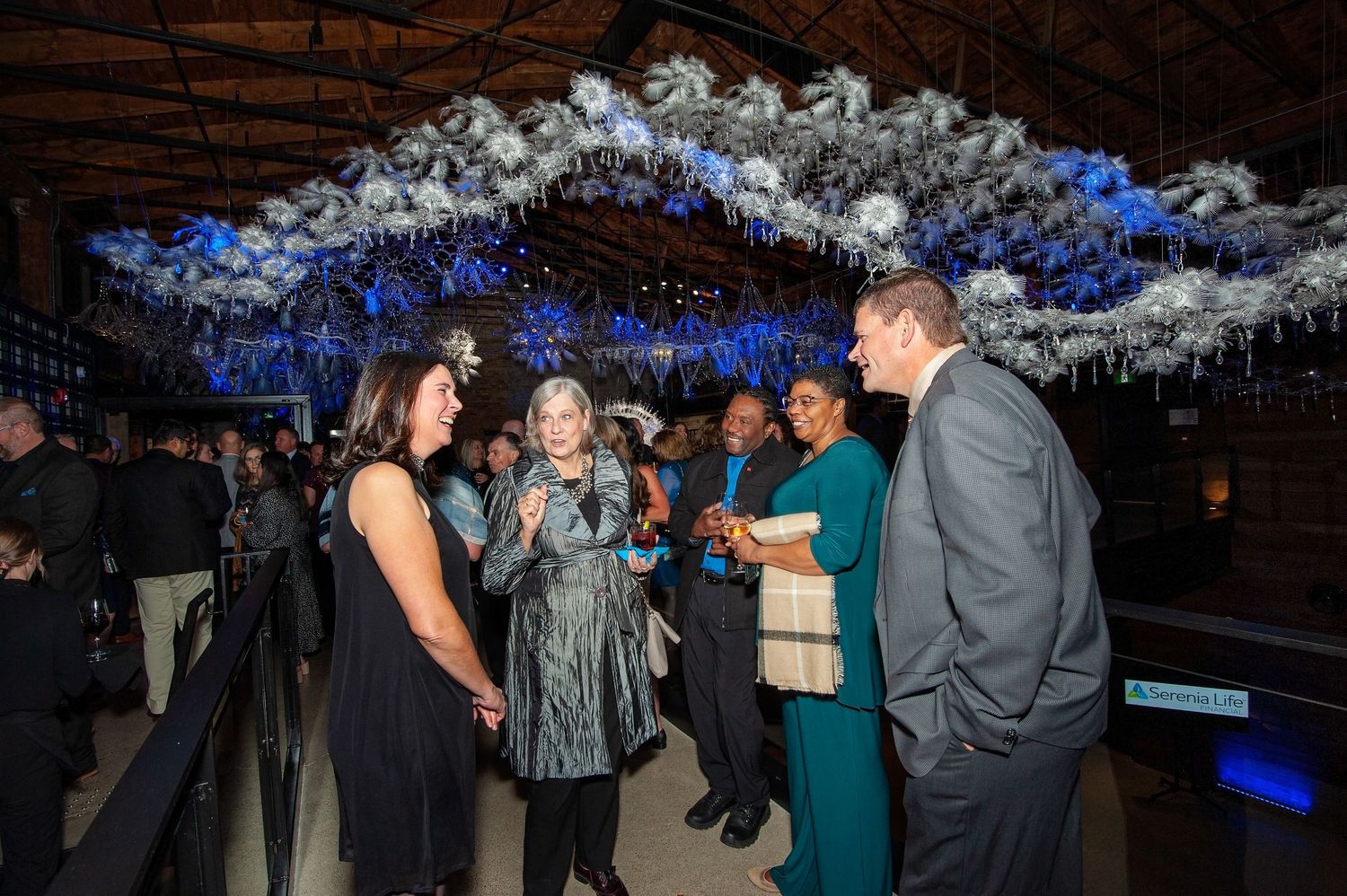 Guests mingle at an elegant evening event under a white floral ceiling installation.