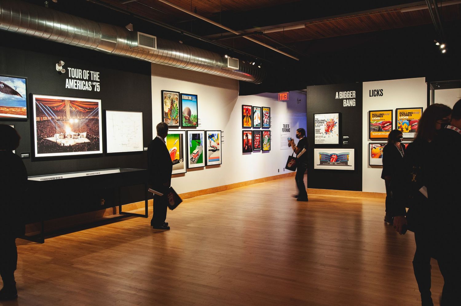 Visitors browse colorful Rolling Stones concert posters and artwork at a music exhibition gallery.