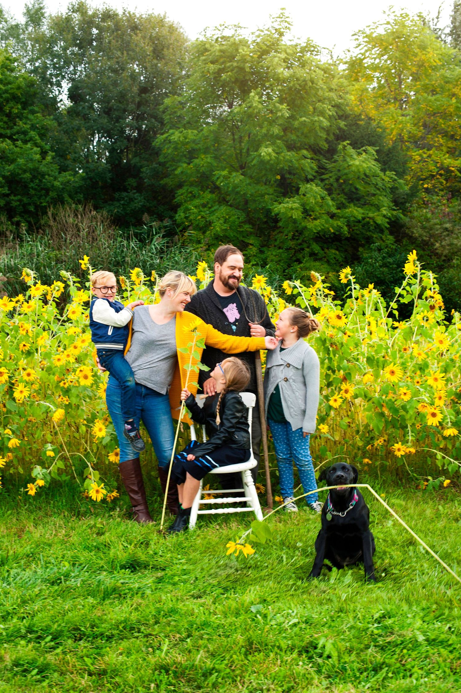 Happy family with black labrador posing together in front of yellow sunflower field outdoors.