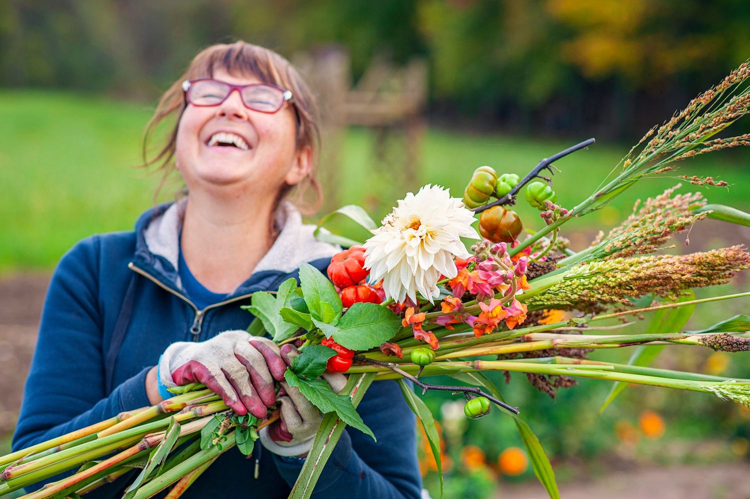 Happy woman laughing while holding a large bouquet of autumn flowers and foliage outdoors.