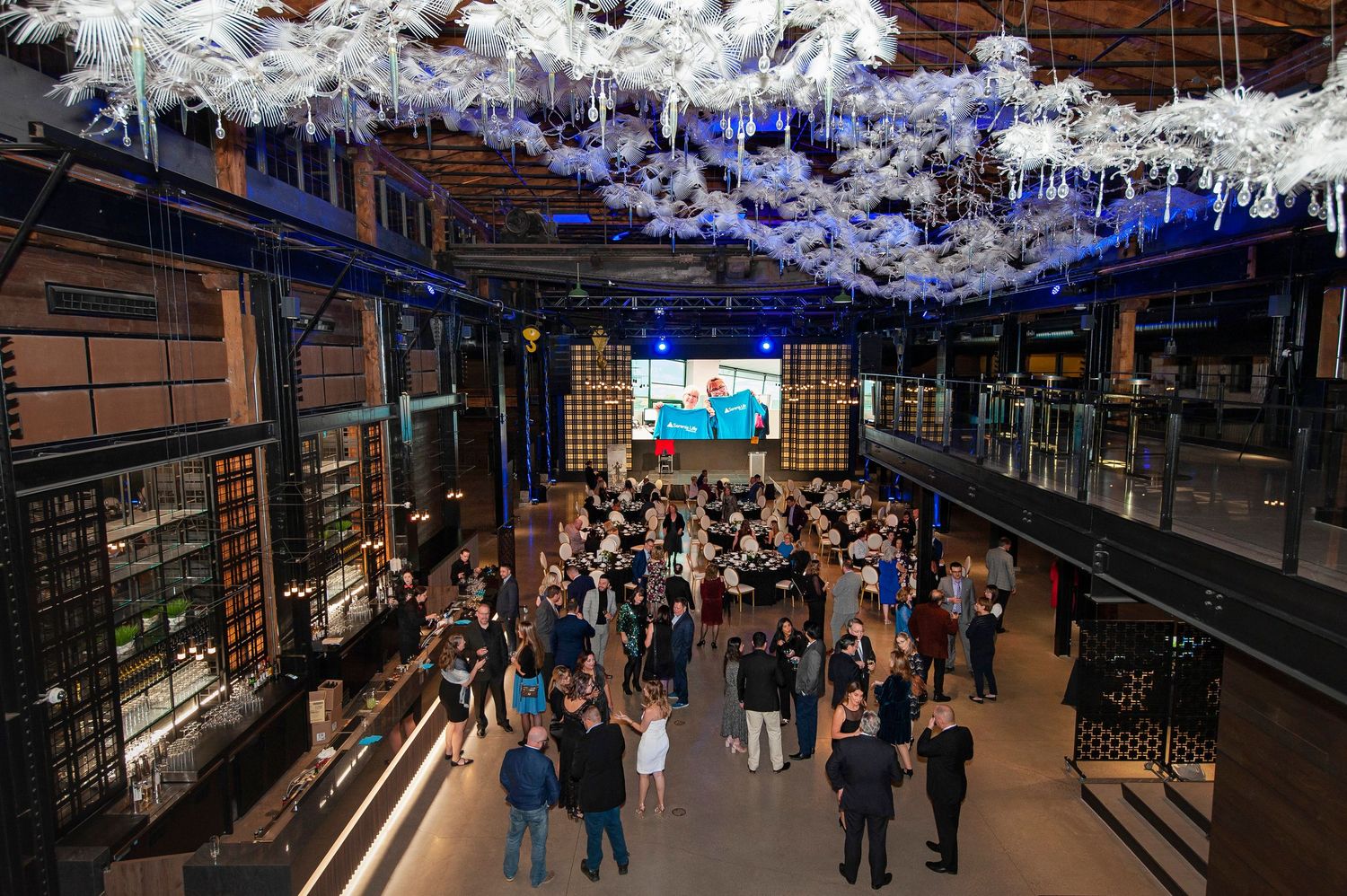Aerial view of a large elegant indoor event venue with white floral ceiling decor and crowd.