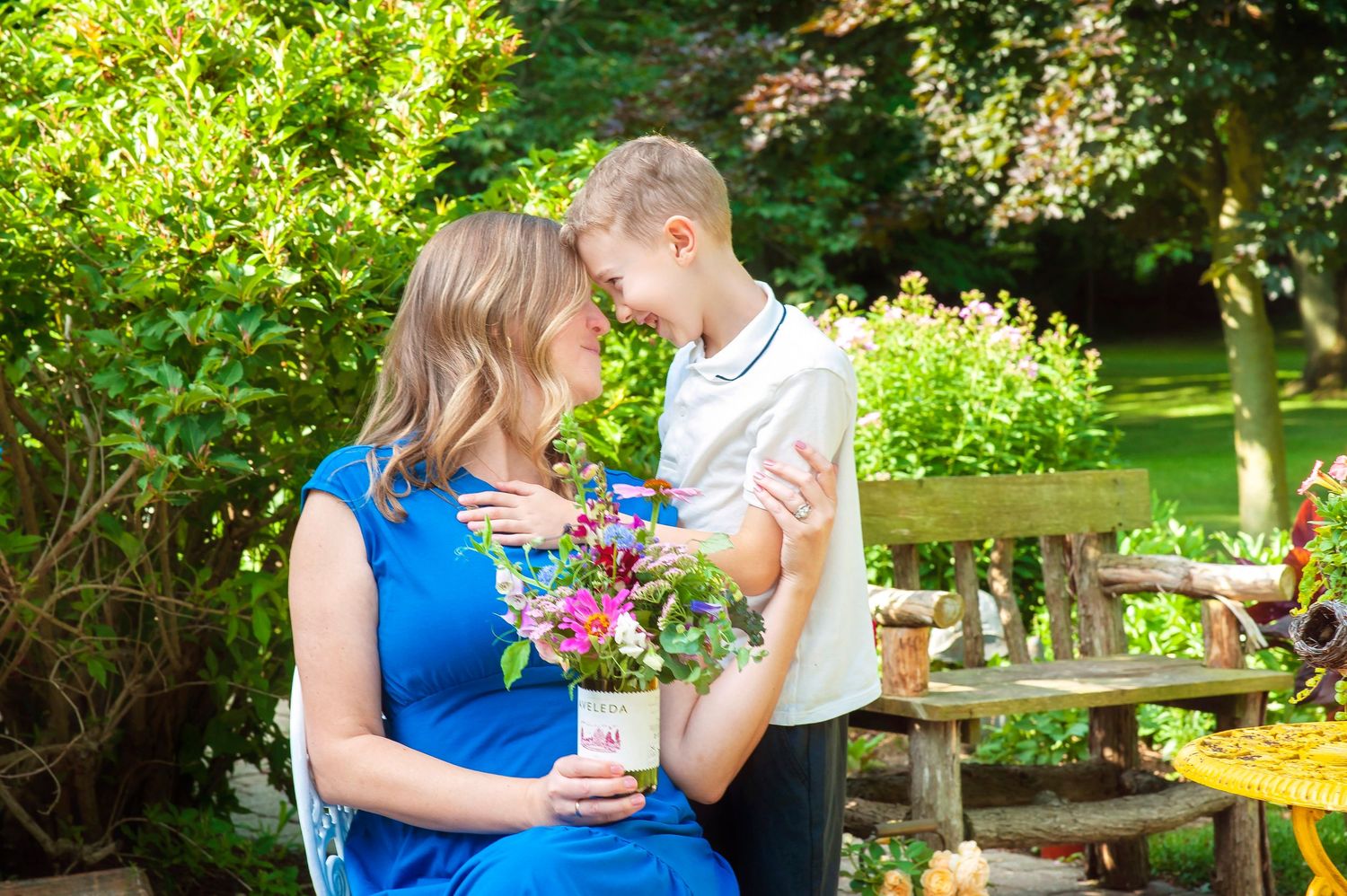 Mother and son holding flowers in a garden.
