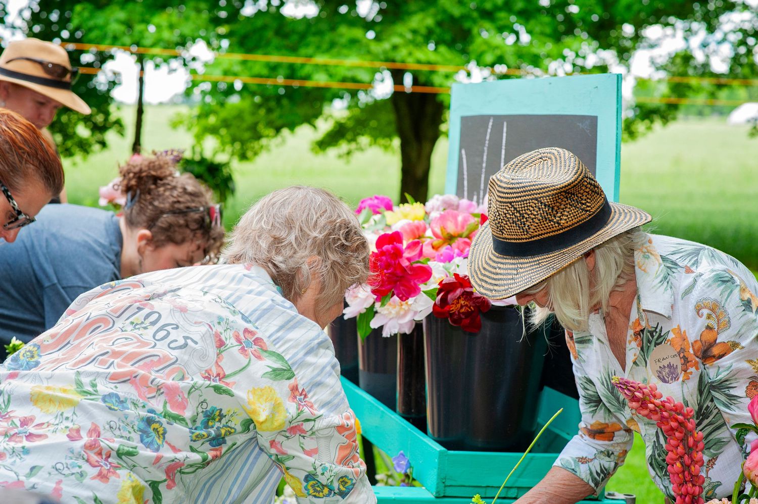 People selecting vibrant pink and yellow flowers at outdoor floral arrangement station in garden.