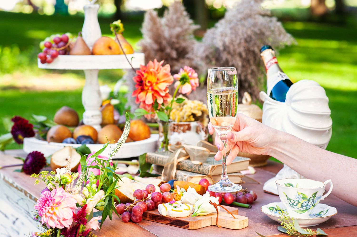 Outdoor garden party table with champagne, cheese, grapes, flowers, and elegant decorations.