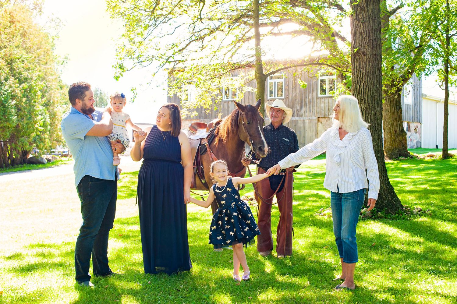 Family with young children and a horse gather outdoors on sunny green lawn near historic building.
