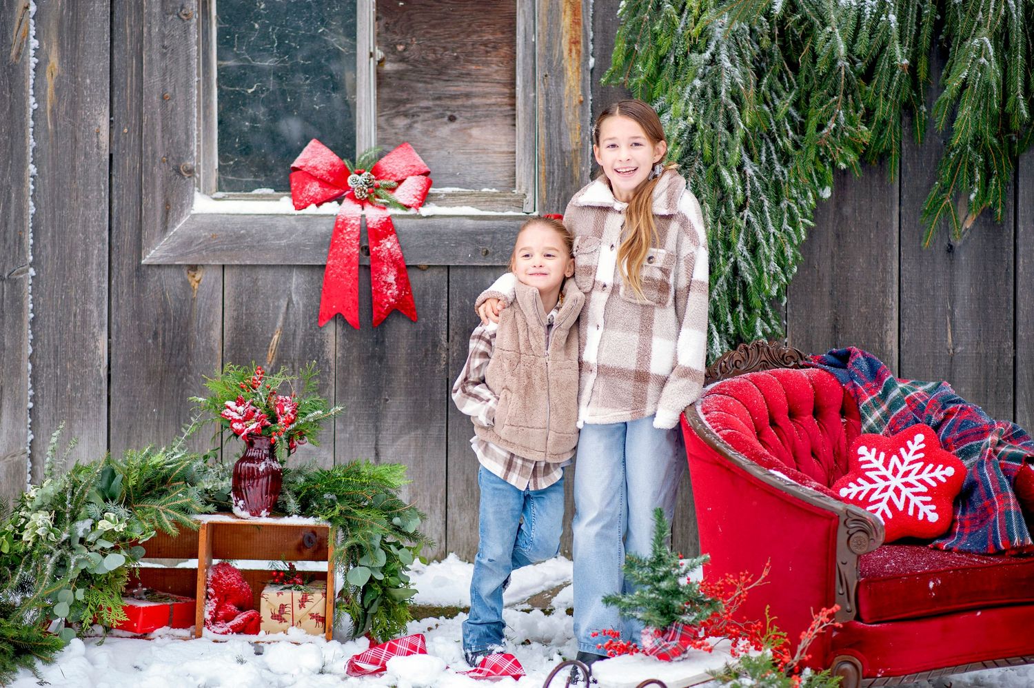 Two children posing in front of rustic Christmas decorated porch in snow.