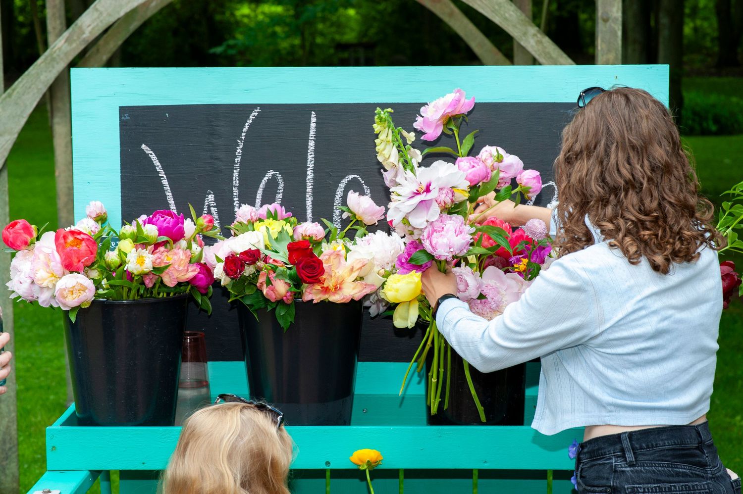 Young woman arranging colorful fresh cut flowers in black buckets on turquoise display table.