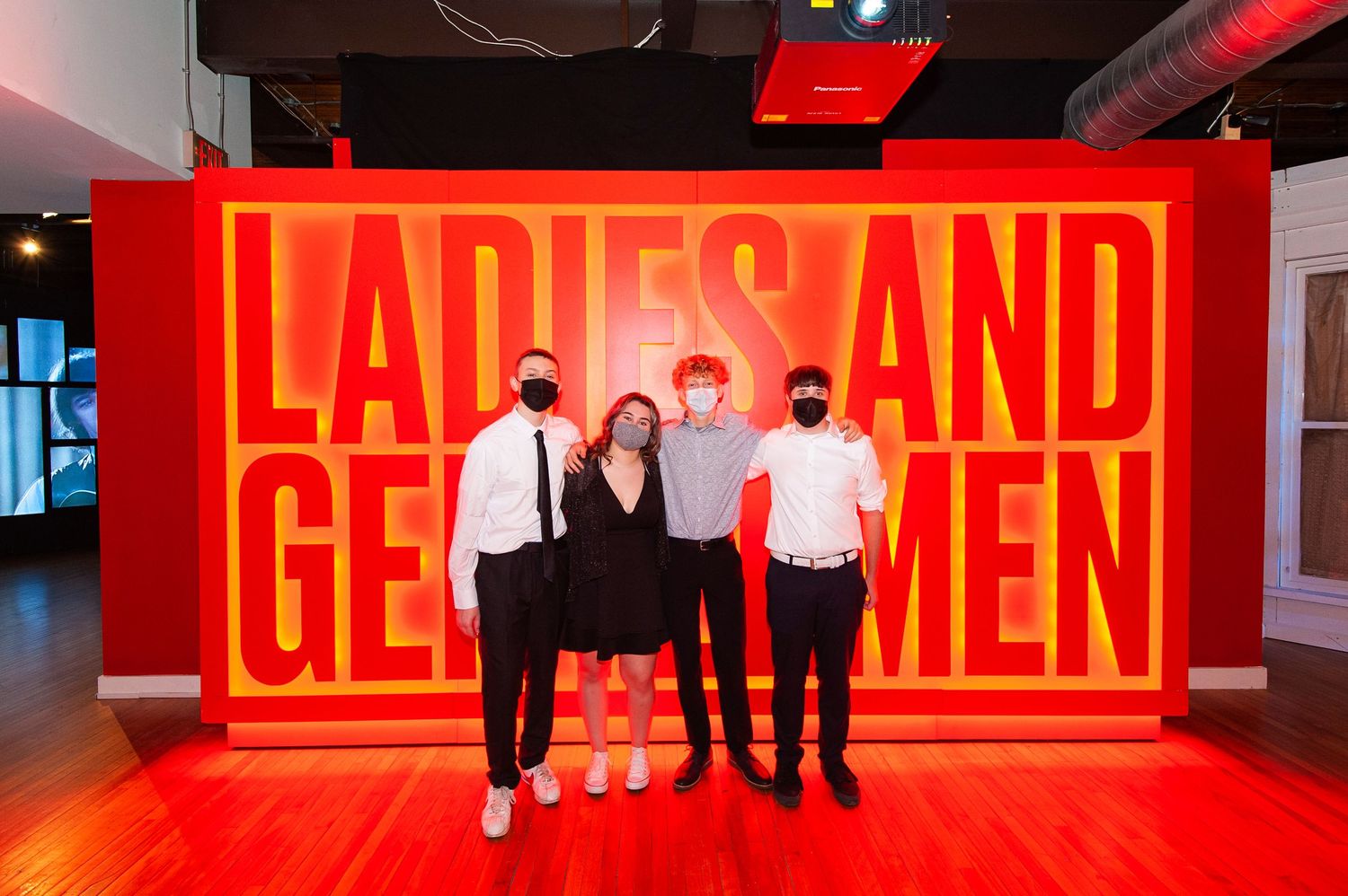 Four people pose in front of a bold red Ladies and Gentlemen sign at a museum exhibit.