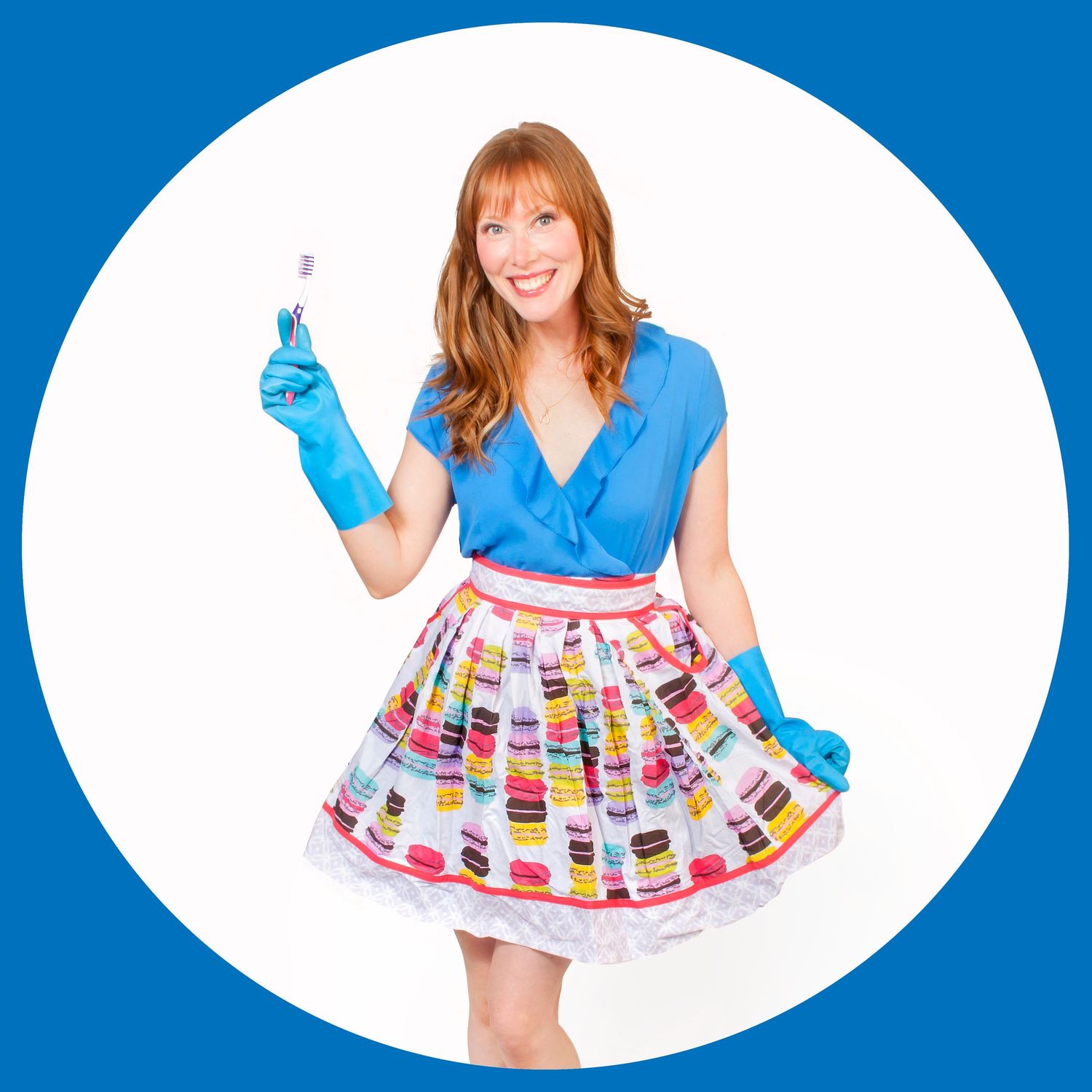 Redhead woman in blue top and macaron-print skirt holding a toothbrush with blue gloves.
