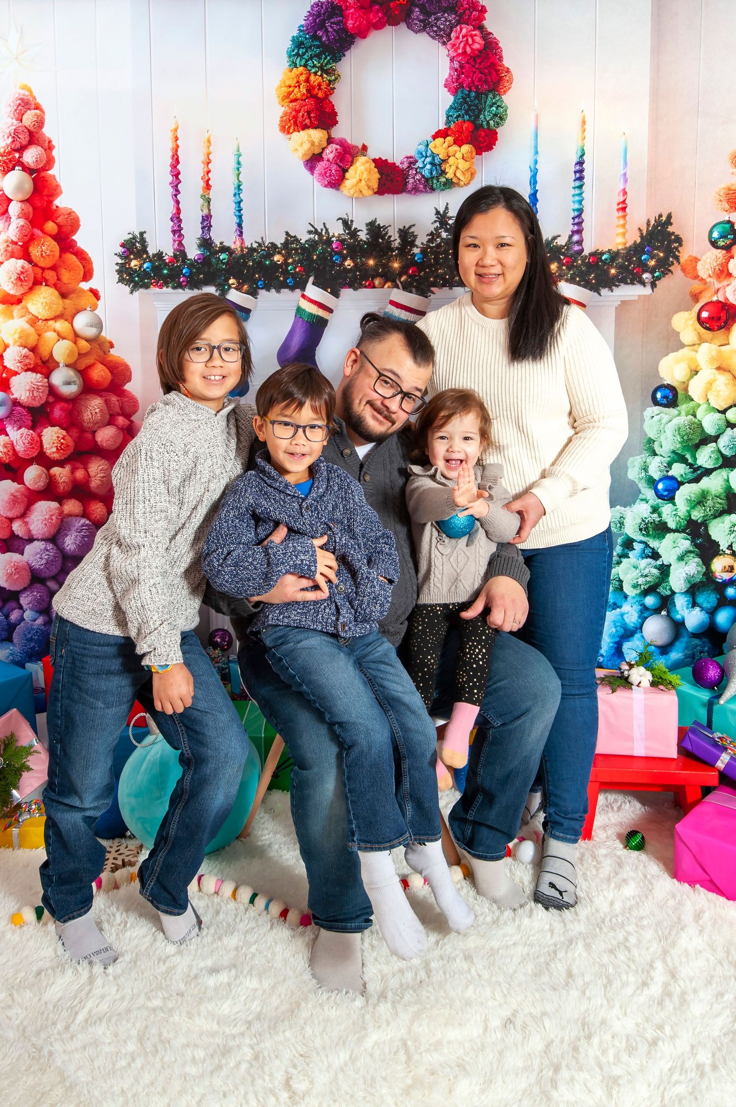 Happy family of five posing together in front of rainbow Christmas trees and festive decor.