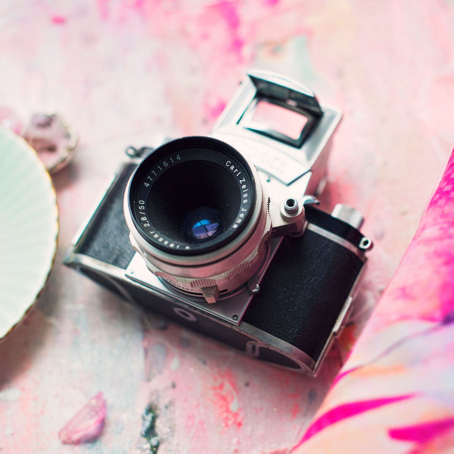 Vintage silver film camera with black leather body resting on a pink painted surface with floral accents.