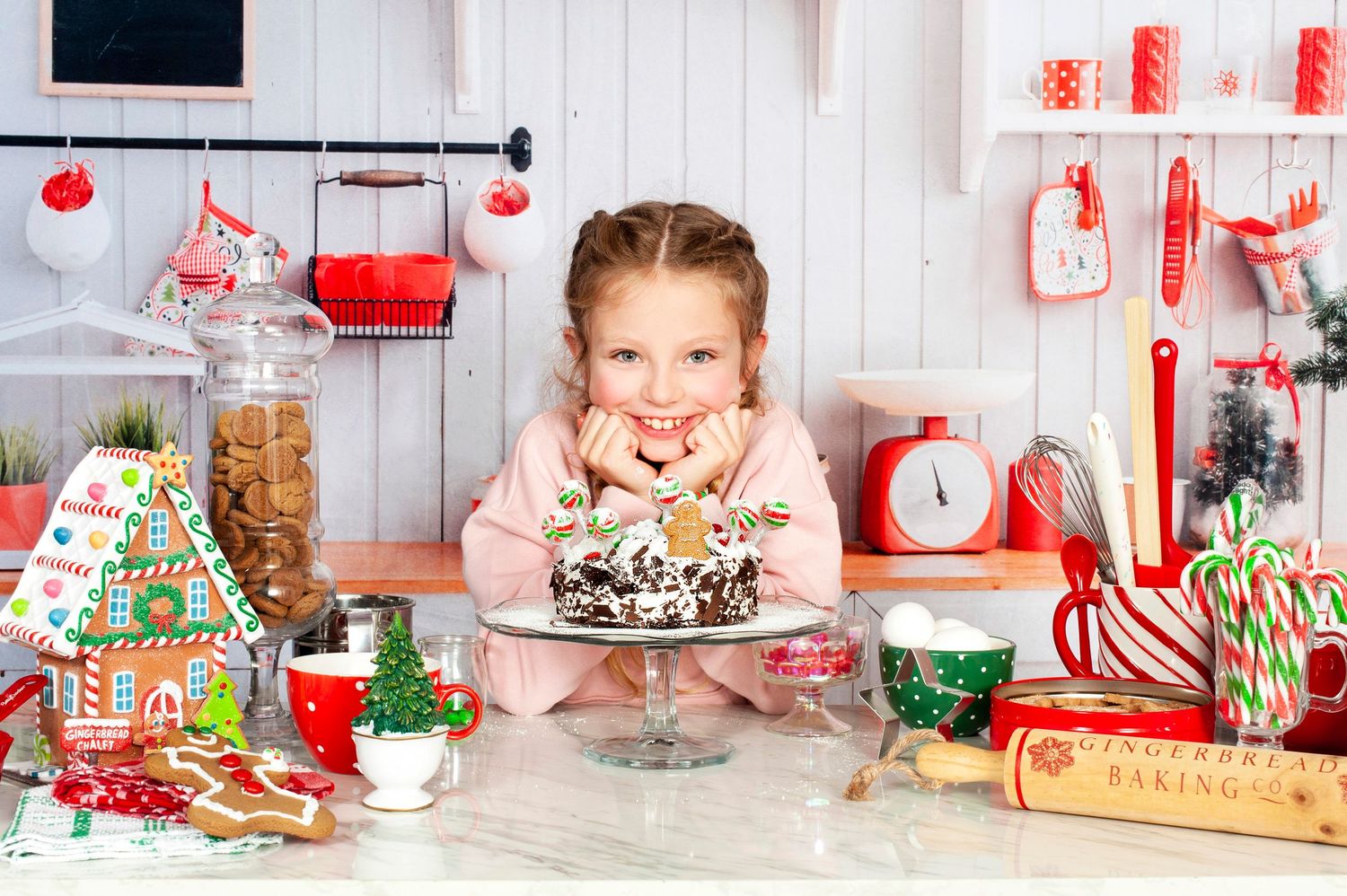 Happy young girl leaning over a Christmas cake surrounded by festive holiday baking decorations and treats.
