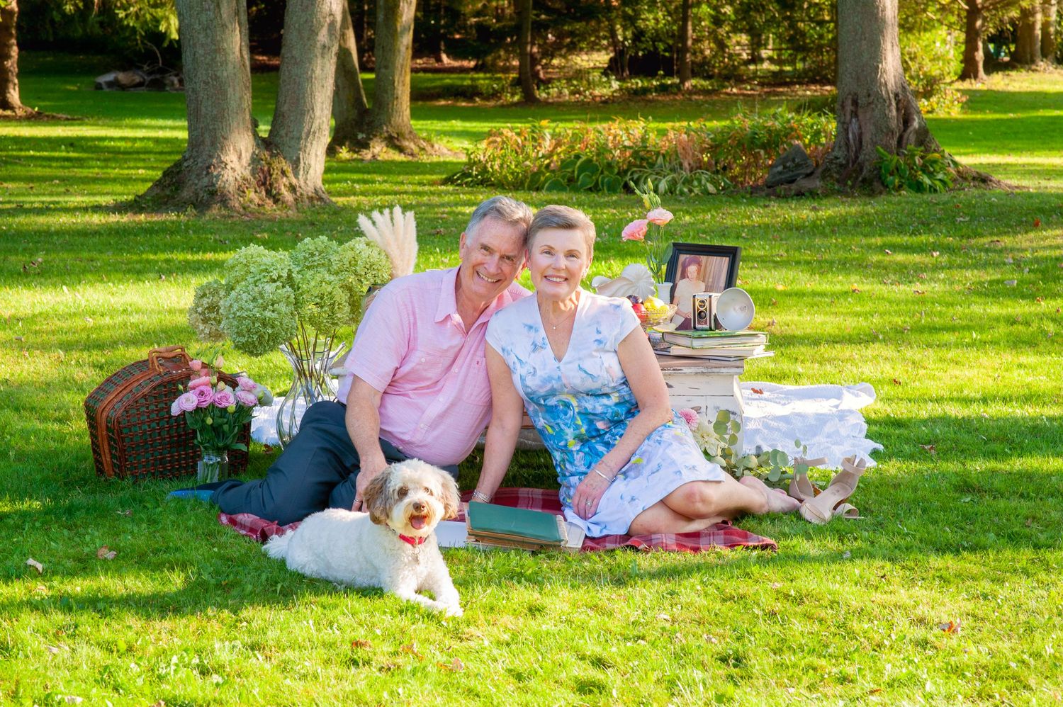 Smiling couple relaxing on grass with golden dog during outdoor picnic in park.