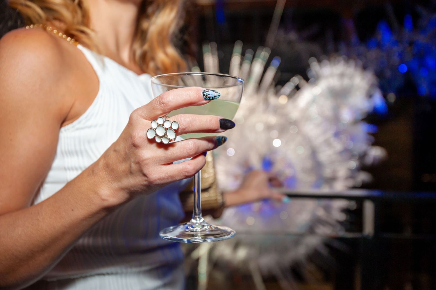 Close-up of a hand with floral ring holding a martini glass at an elegant evening event.