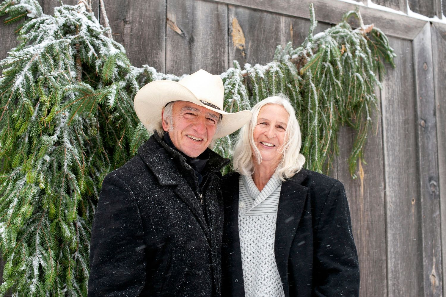 Smiling couple in winter attire posing outdoors in light snowfall.