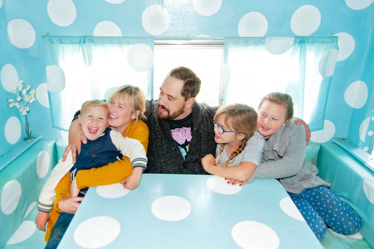 Family sitting together inside turquoise polka dot caravan at table.