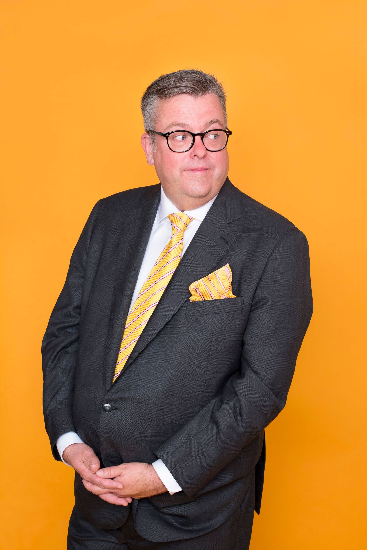 Professional man in gray suit with yellow tie and pocket square on orange background.