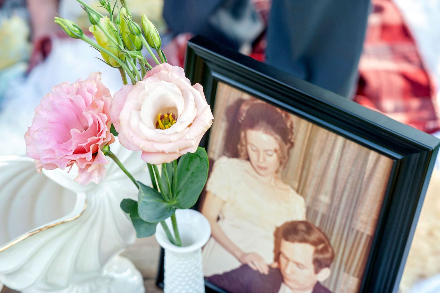 Vintage framed photo beside pink roses in white vase on decorated table.
