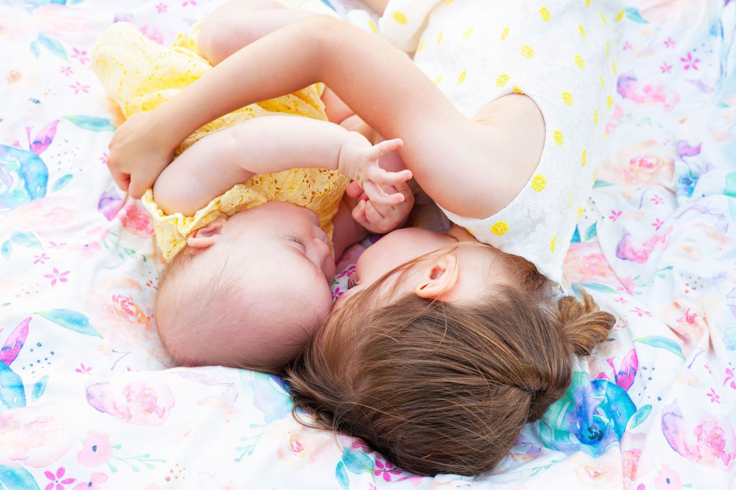 Two young siblings lying together on colorful floral blanket in matching outfits.