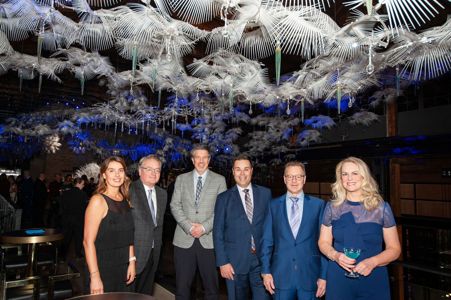 Six professionals posing under elegant white floral ceiling installation at a formal evening event.