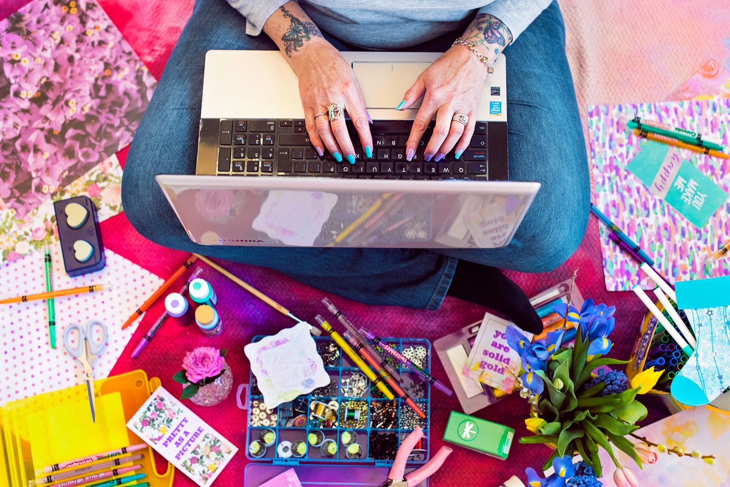 Overhead view of woman using laptop surrounded by colorful stationery and office supplies.