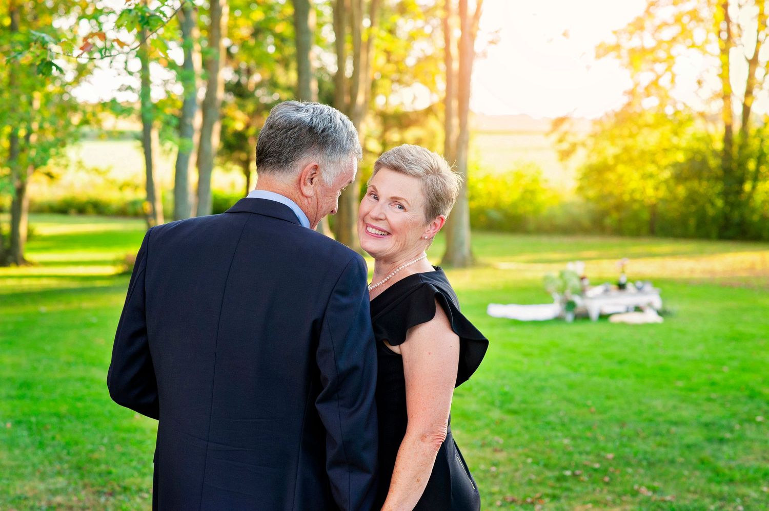Elegant couple dancing outdoors in golden sunlight among green trees.