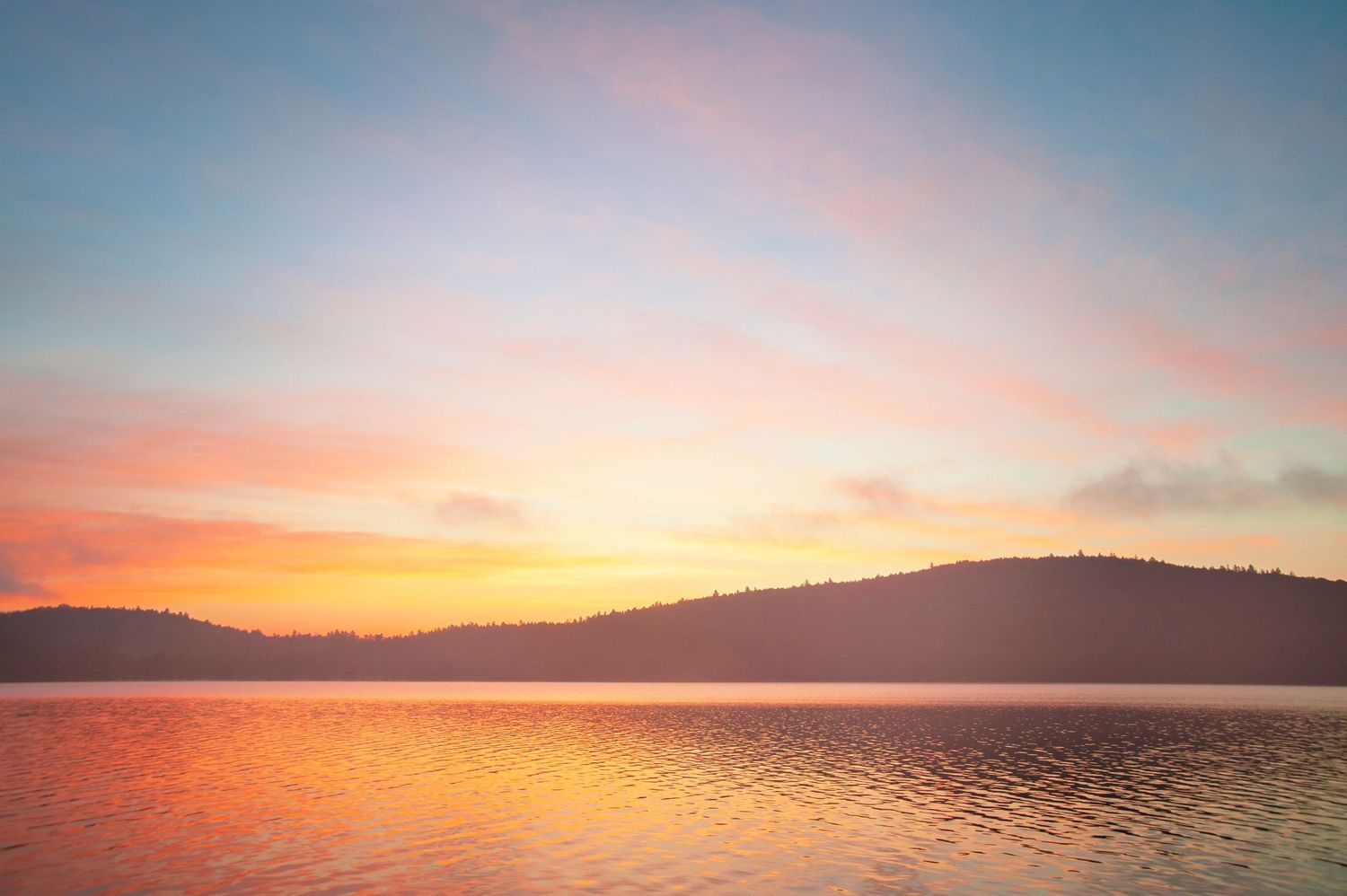 Stunning sunset over a calm lake with vibrant orange and pink sky reflecting on the water and silhouetted hills.