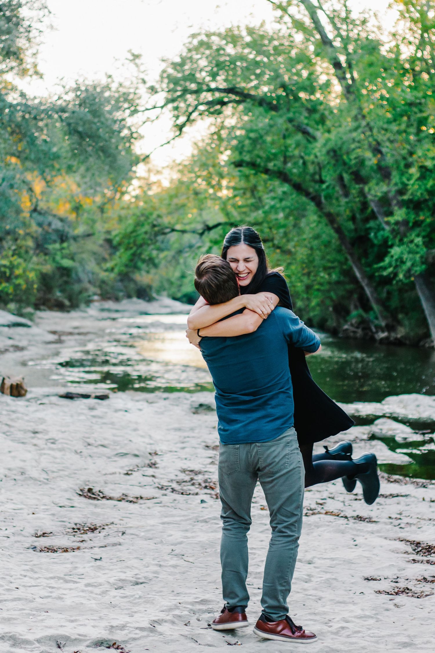 Candid outdoor photoshoot sequence showing playful interaction on a sandy riverbank surrounded by green trees.