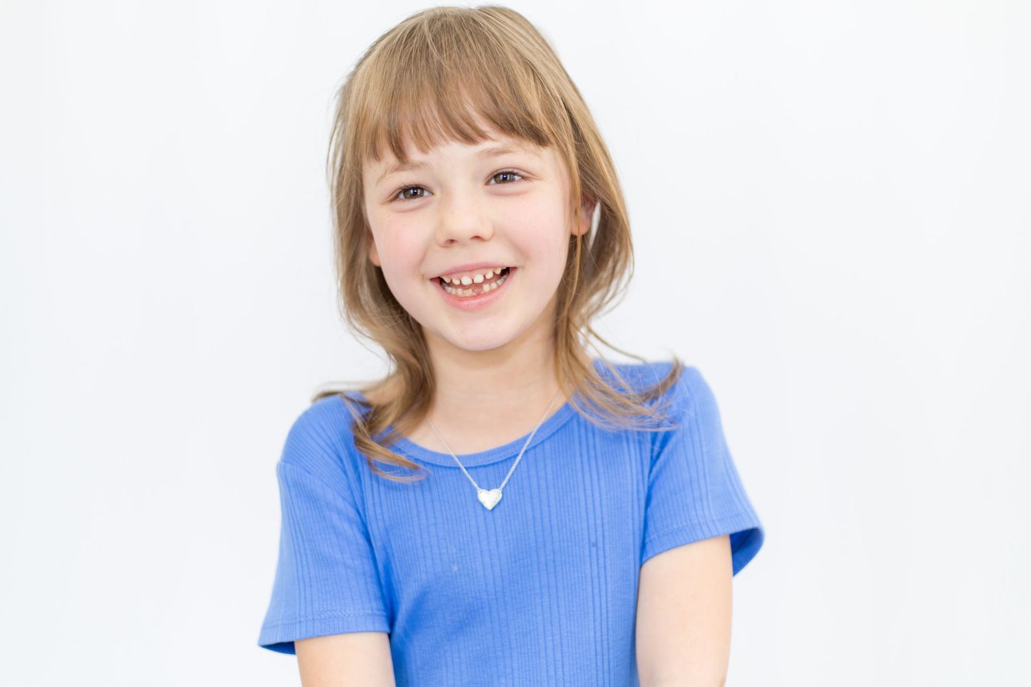 Child in blue ribbed top poses cheerfully against white backdrop.