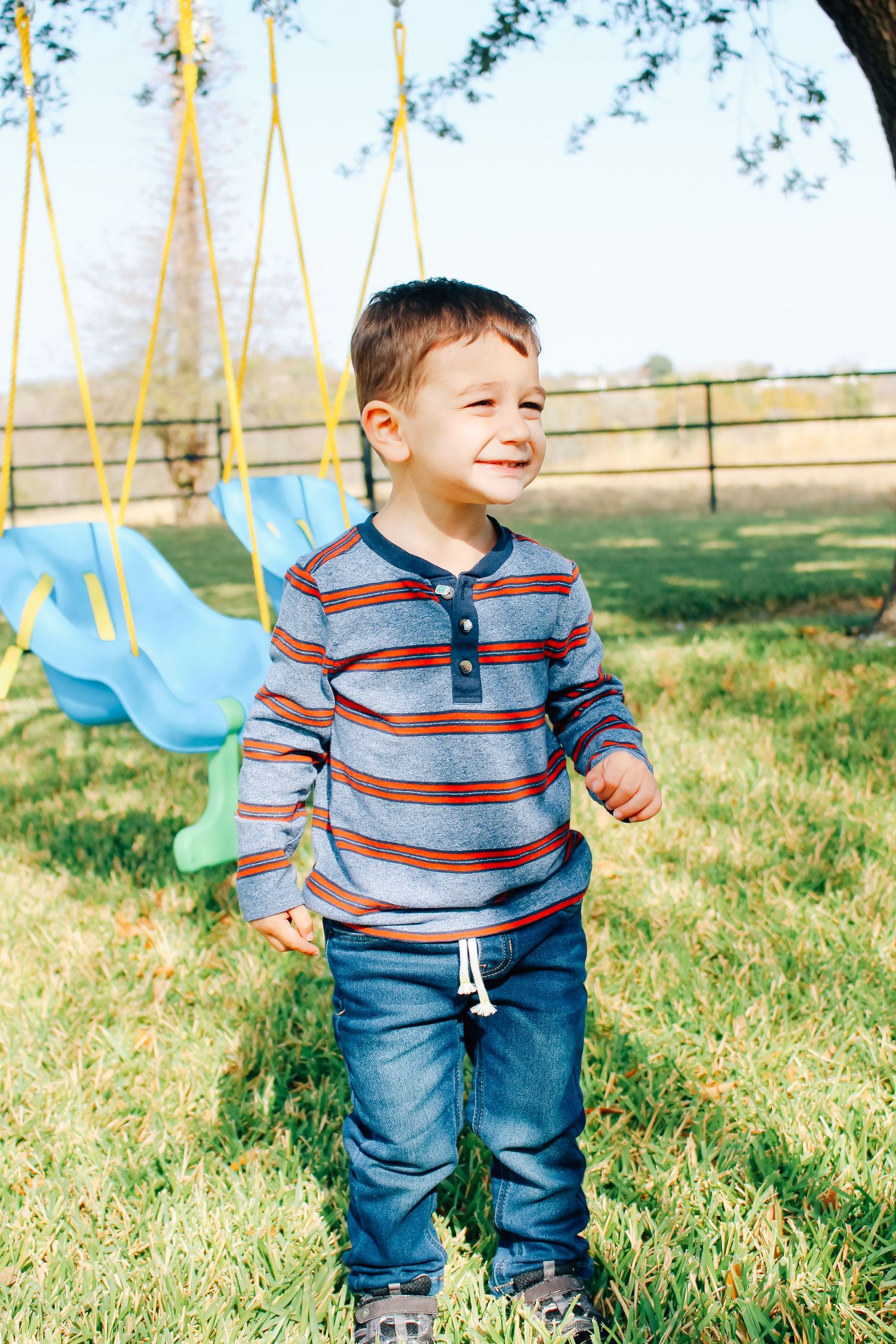 A small child wearing stripes and jeans plays joyfully in a grassy outdoor area.