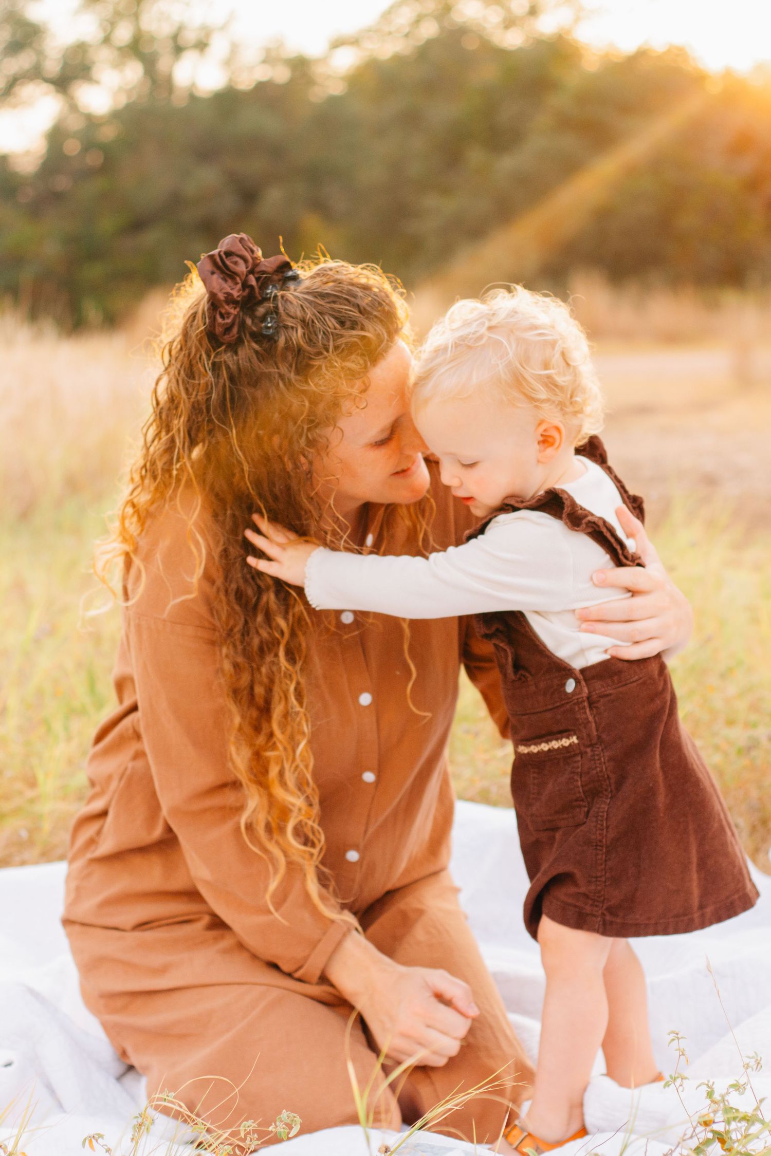 Intimate family moment captured in golden sunlight on a white blanket outdoors.