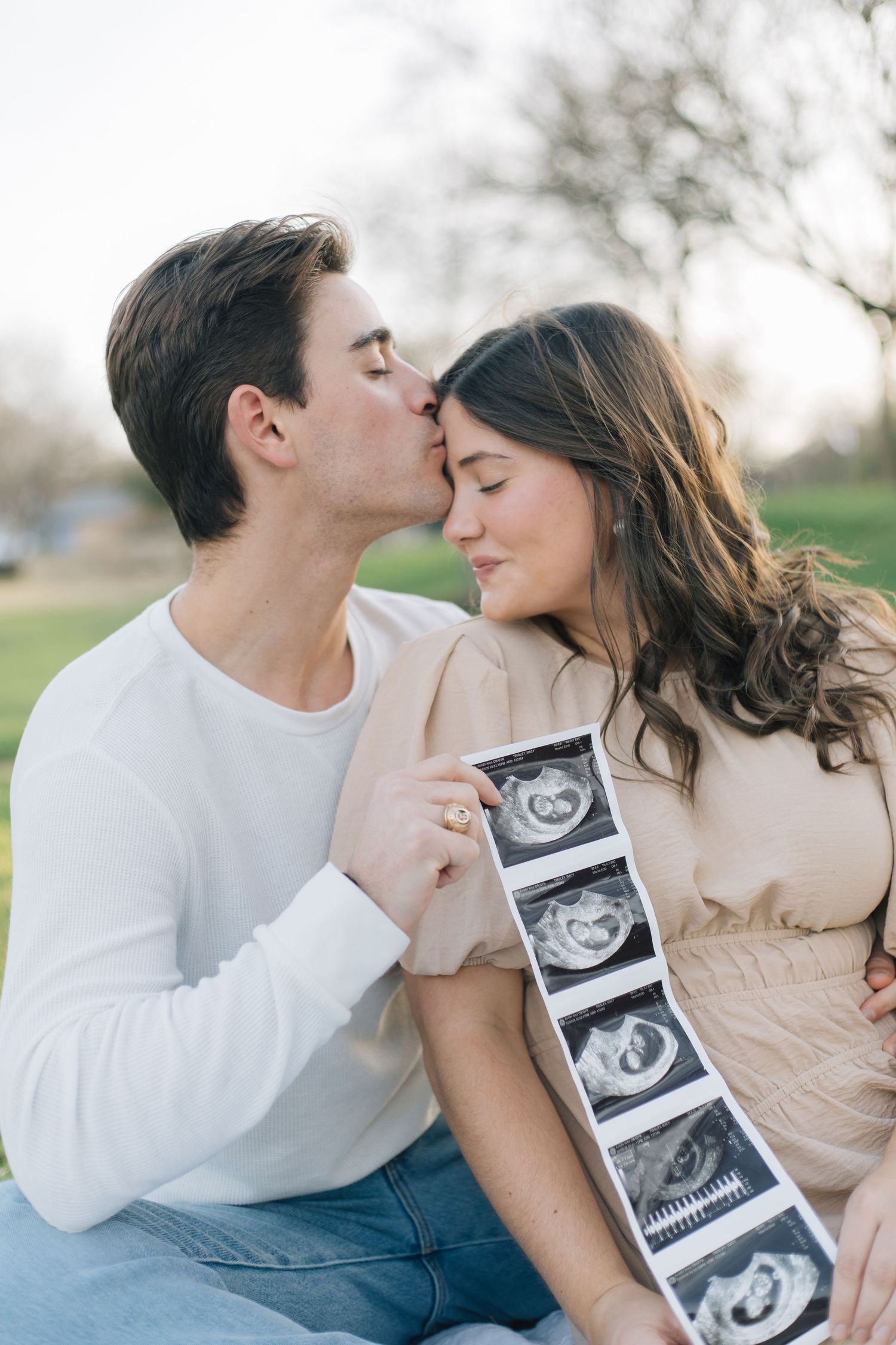 Intimate outdoor moment between couple sharing tender moment with ultrasound photos.