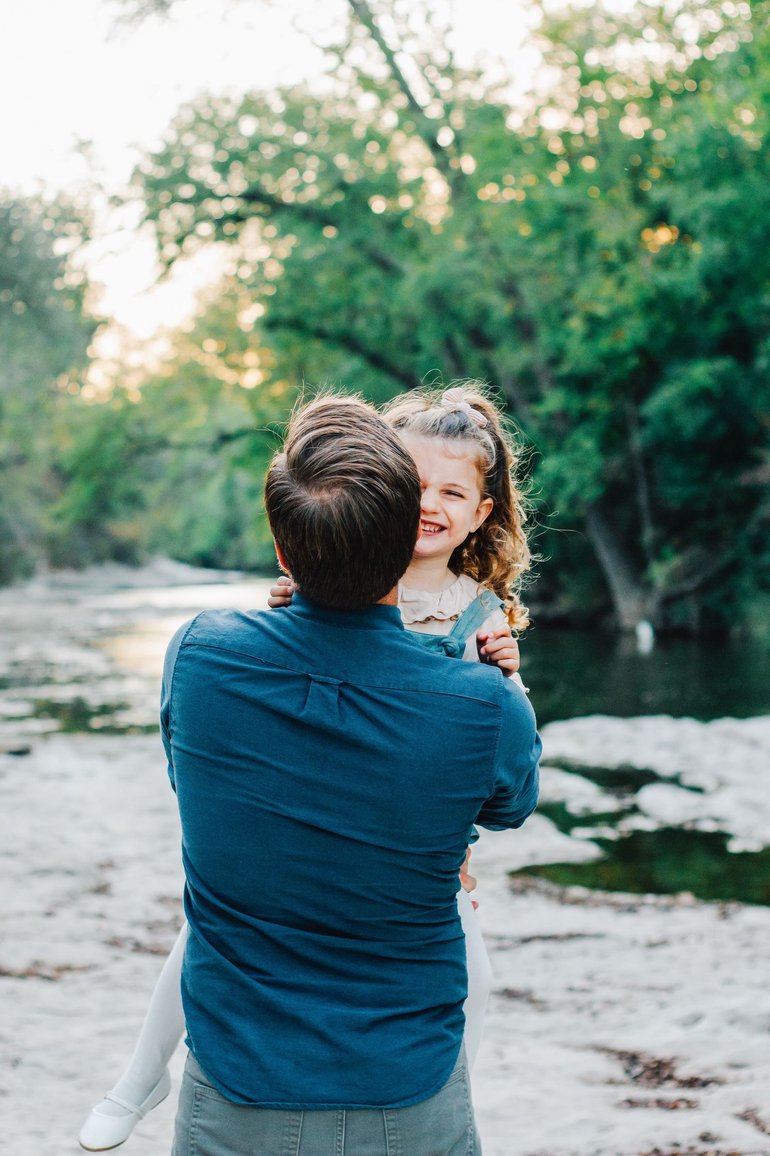 Couple shares intimate embrace by riverside during outdoor photo session.