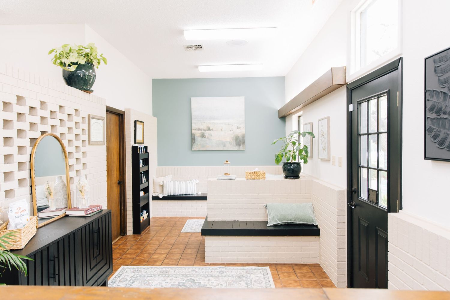 Bright modern salon interior with teal accent wall, black cabinetry, terracotta floors, and minimalist decor.