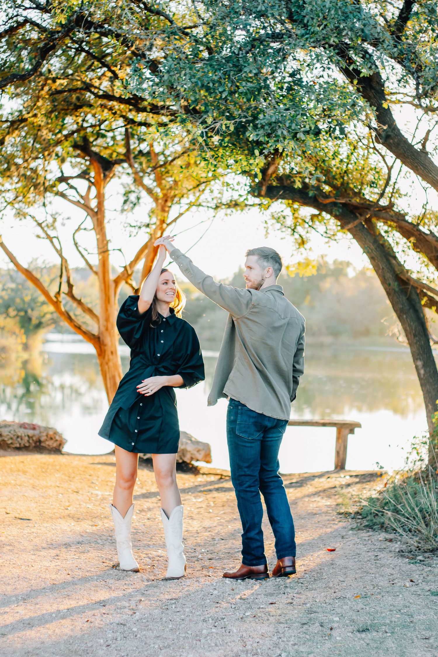 Playful couple interacts with their dog on a dirt path under golden autumn trees.