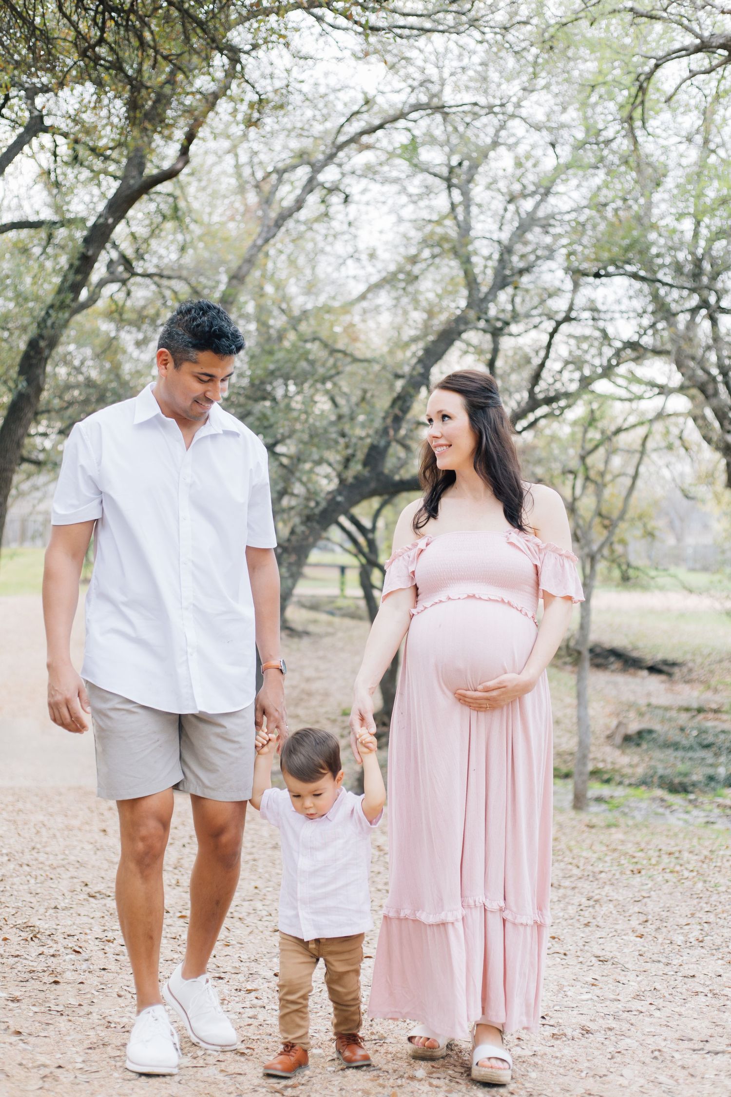 Family walking together outdoors wearing coordinated pink and white outfits among trees.