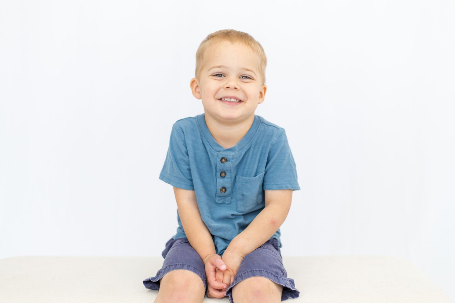 Toddler in blue t-shirt and navy shorts smiles during studio session.