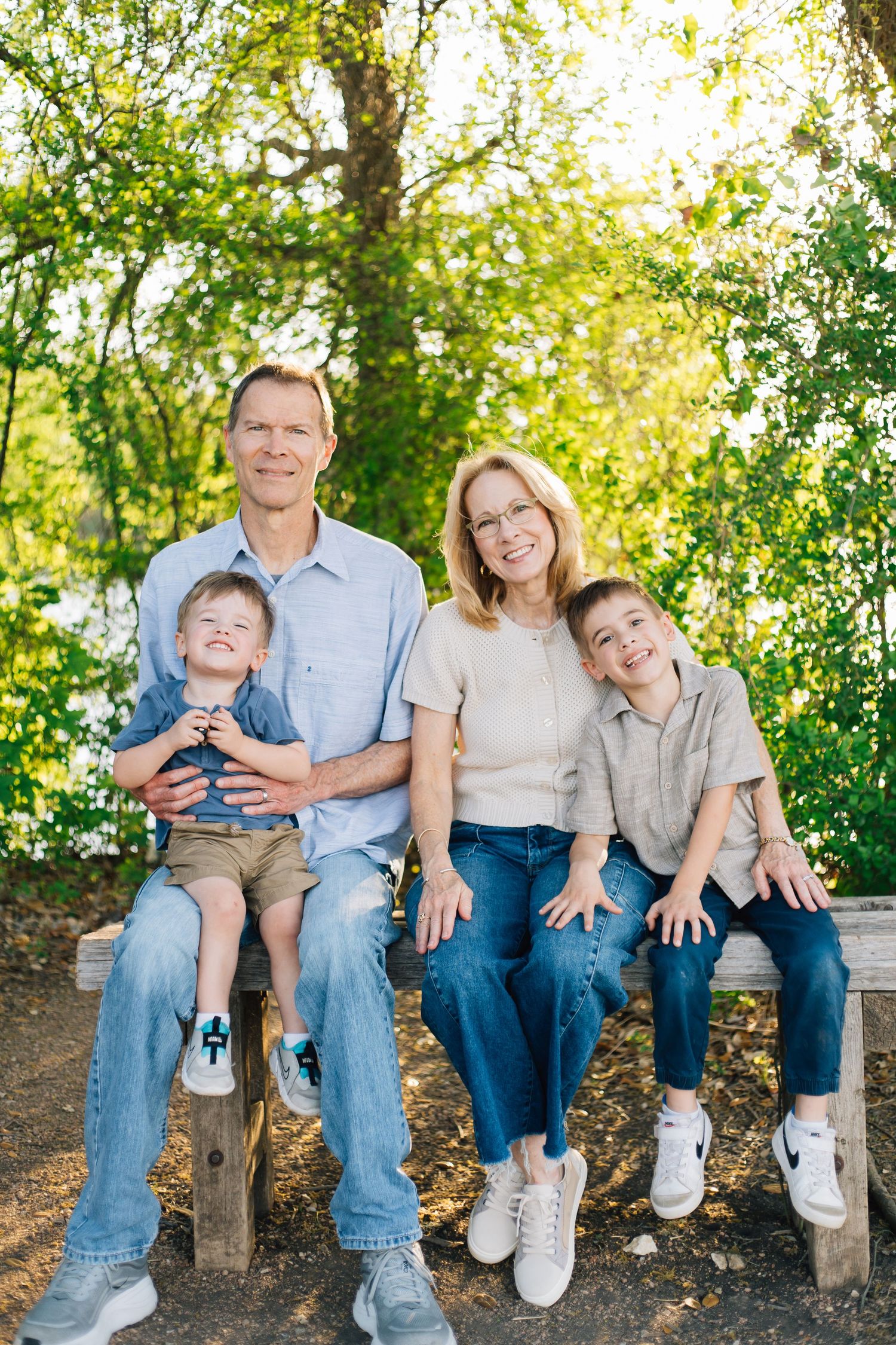 Grandparents sitting on a wooden bench with two young grandsons in a lush green park.