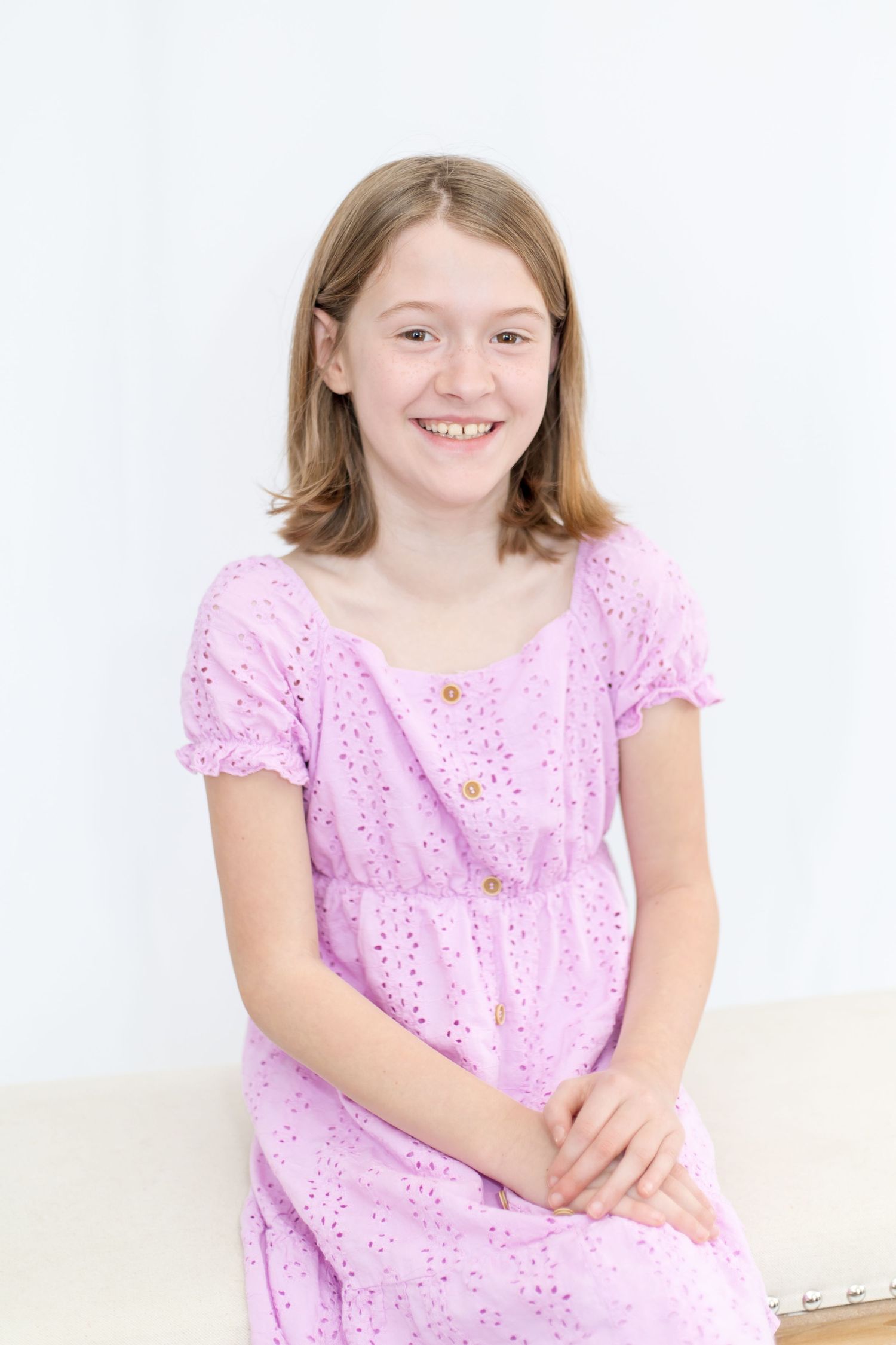 Studio portrait in pink eyelet lace dress against white background.