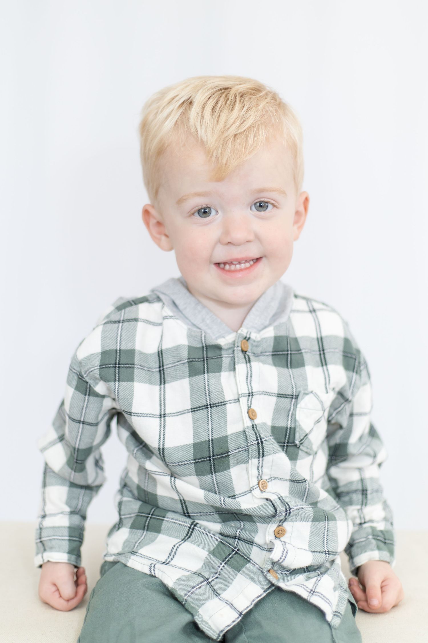 Young child wearing green plaid shirt and pants smiling at camera.