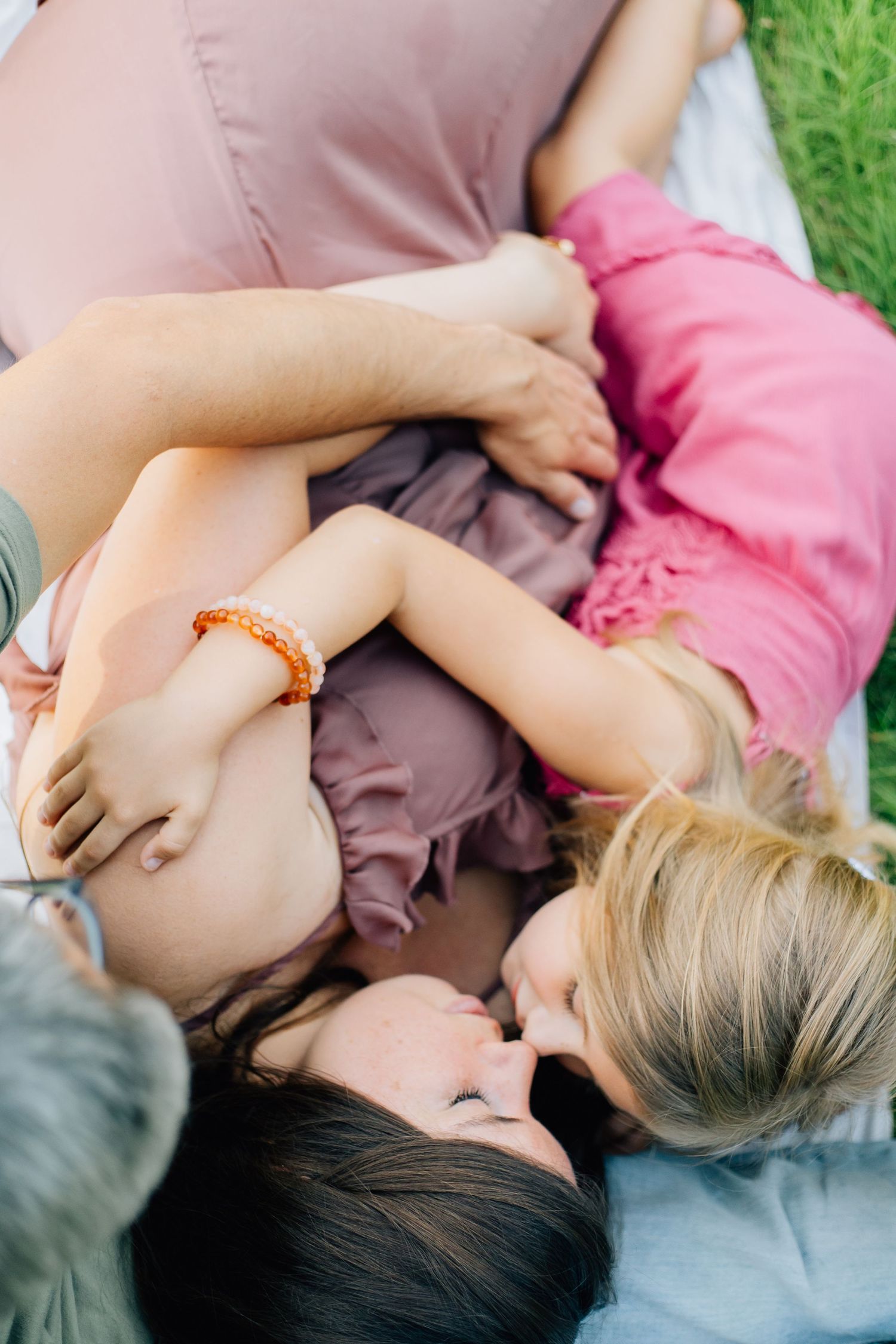 Overhead view of pregnant mother and young daughter lying together on blanket in green grass.