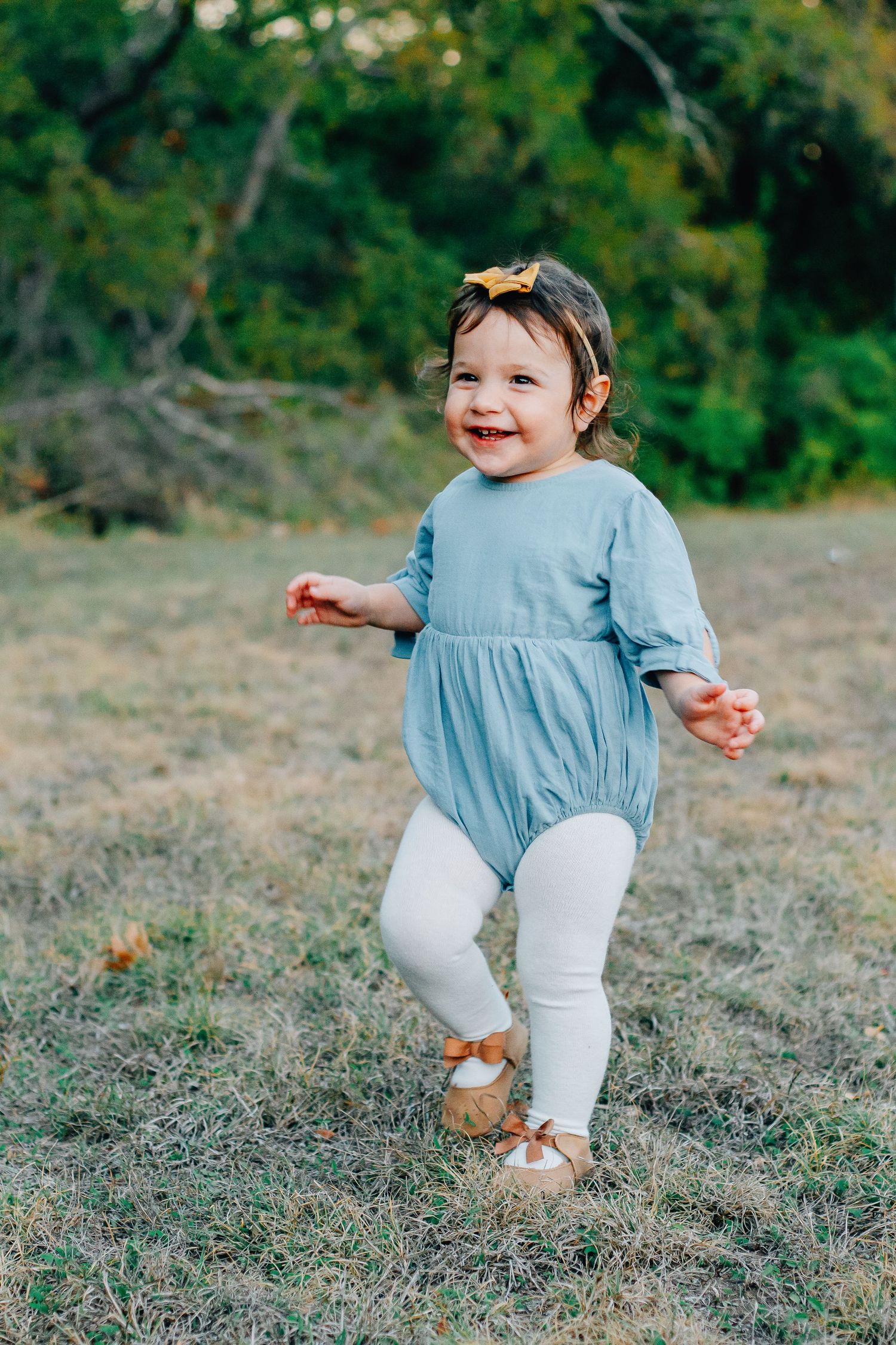 Playful toddler in blue outfit exploring and walking through grass during outdoor photo session.