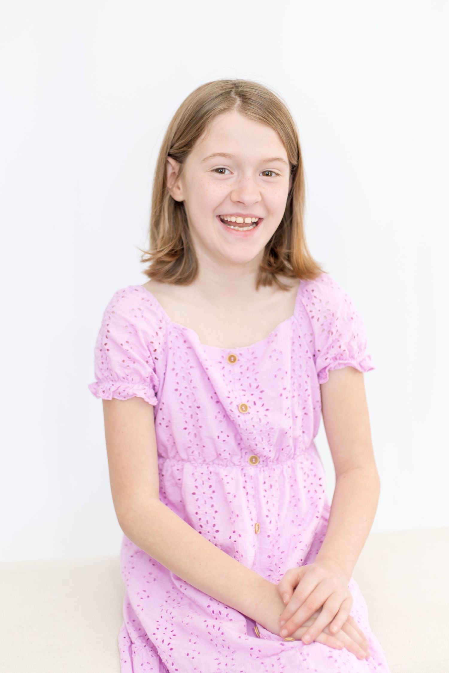 Young girl in pink eyelet dress sitting against white background.